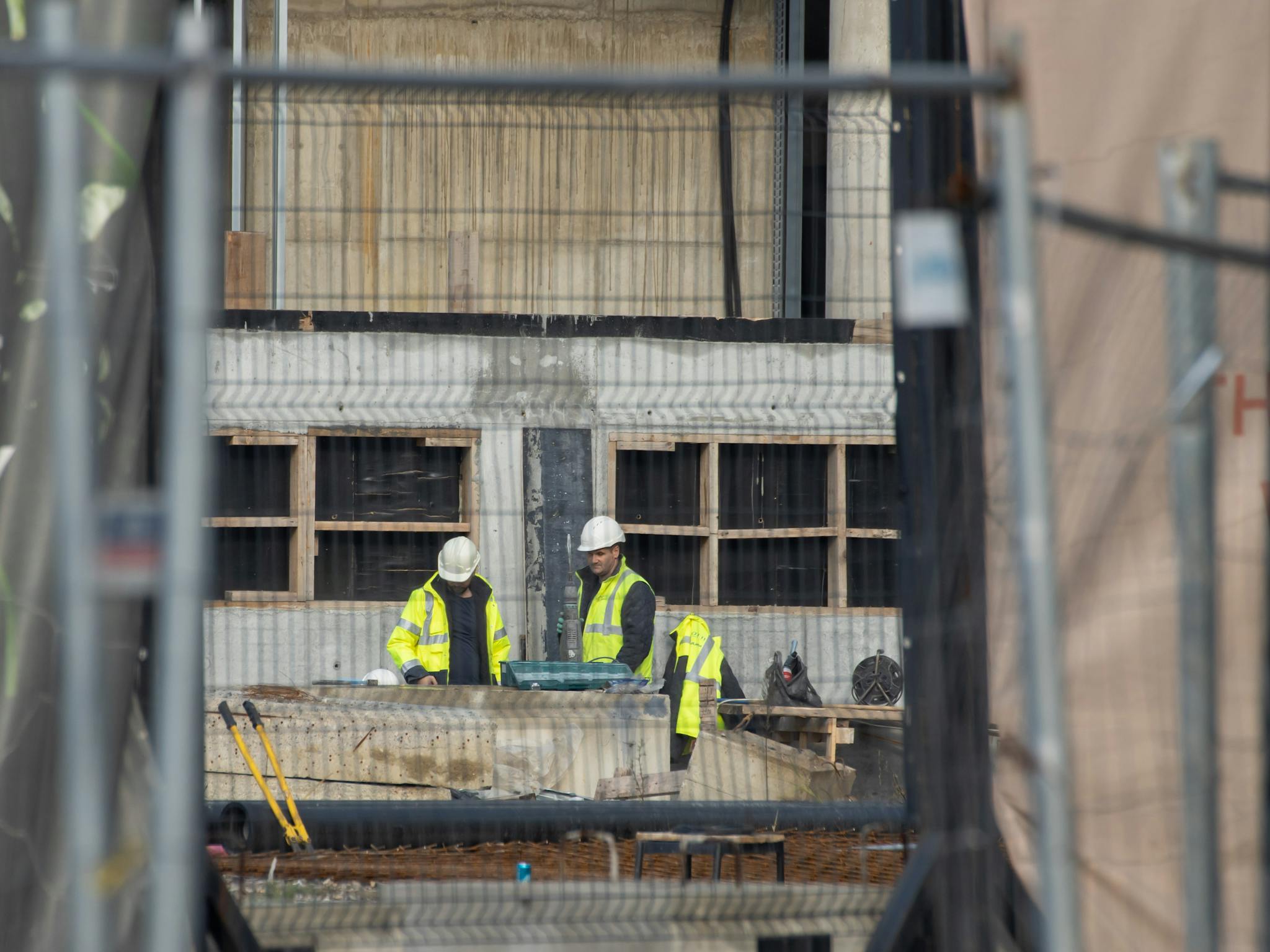 Two construction workers wearing safety gear collaborate on a building site, emphasizing teamwork.